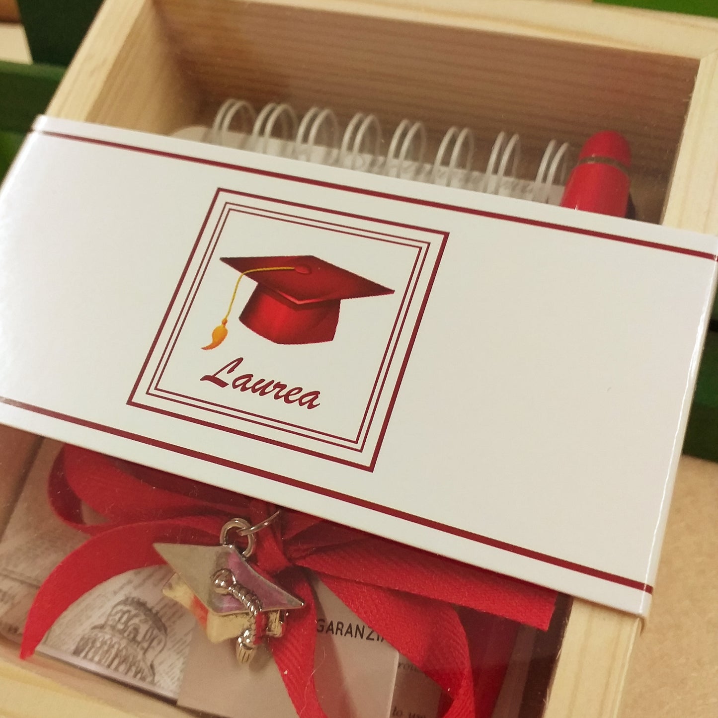 esterno del set di scrittura astuccio legno e plastica scritta laurea penna rossa biro mini block notes ciondolo cappello tocco tubo portaconfetti confetti rossi coccarda nastro confezionata artigianale