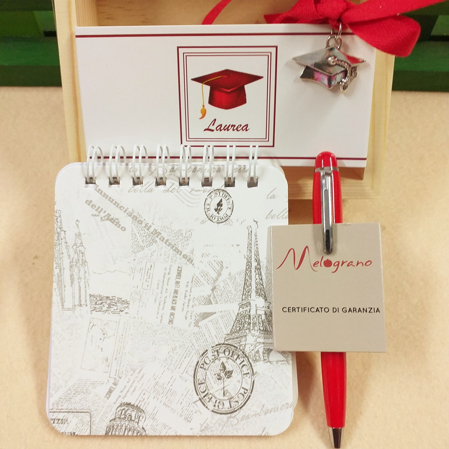 cosa contiene il kit di scrittura bomboniera laurea block notes copertina mini penna rossa Melograno certificato di garanzia cartoncino laurea ciondolo cappello tocco astuccio di legno