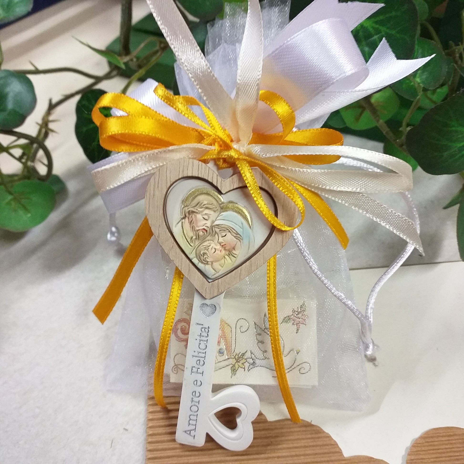 primo piano scritta frasi Amore e Felicità su oggettino packaging sacchetto bianco nastri giallo oro girasole confezionato confetti bigliettino bomboniera Prima Comunione Santa Cresima Battesimo matrimonio icona Sacra Santa famiglia chiave ricordino religioso legno e ceramica