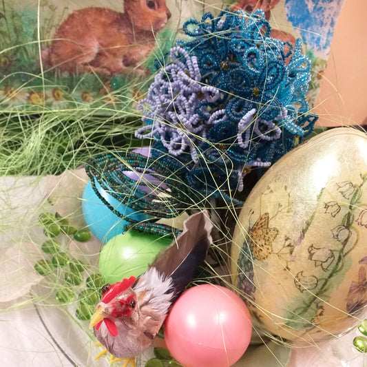 primo piano scena animali del piatto di vetro idea regalo centrotavola pasquale ortensia fiori di perline azzurri blu ovetti di plastica gallo piume decorazioni addobbi petali sassolini vetro uovo grande mughetti violette sfondo vetrina runner coniglietti