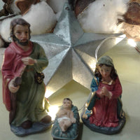 idee natale fai da te con gruppo di statuine Sacra Famiglia rappresentazione del Presepe Natività statuette colorate piccole ambientazione lucine natalizie fiori di cotone stella metallo