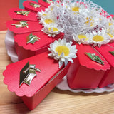 primo piano scatoline a fetta di torta bomboniere confezionate confetti con margherite simboli cappello di laurea su vassoio